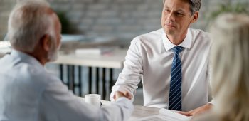 Happy real estate agent and senior clients shaking hands after successful meeting in the office.